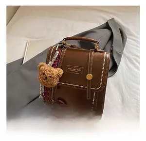 Detail of brown leather backpack with contrast stitching, metal buckle, and bear charm