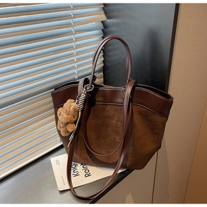 Detail of a dark brown suede tote bag featuring leather patchwork and a plush bear charm