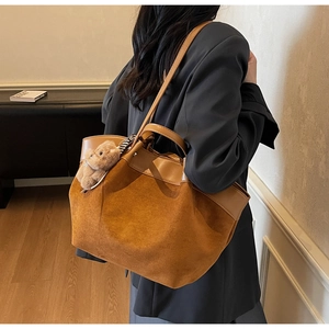 Detail view of brown suede tote bag with leather trim and bear charm on shoulder