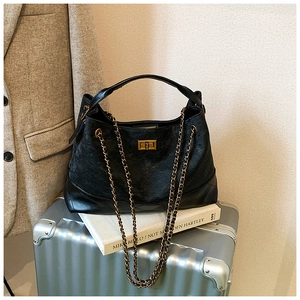 Detail of a large quilted hobo bag with gold chain strap and metal lock on books