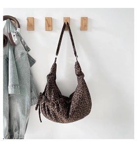 Leopard print crossbody bag with drawstring side detail hanging on a white wall hook