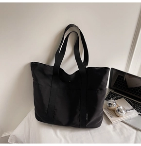 Detail view of large black nylon tote bag with side label on white fabric surface