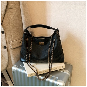 Detailed close-up of a black quilted chain bag with a gold clasp on a travel suitcase
