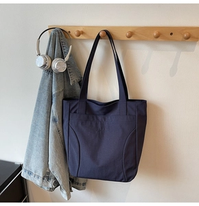 Detail of navy blue canvas tote bag with Midolai embroidery hanging on a wooden hook