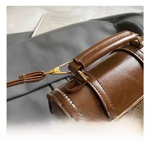 Close-up of golden metal hook and white contrast stitching on vintage brown leather bag