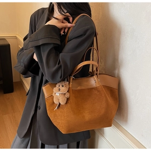 Detailed shot of brown suede tote bag featuring a plush bear charm on a model