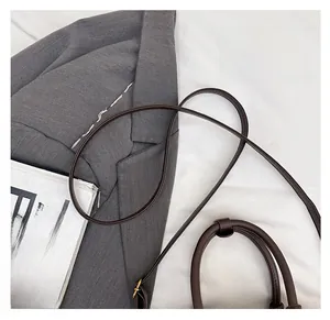 Close-up of matte brown tote bag with round handle and detachable shoulder strap detail