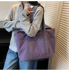 Detail view of the purple nylon tote bag featuring wide shoulder straps and side brand label