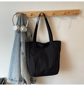 Detail of black tote bag with curved stitching and embossed logo on minimalist wall hook
