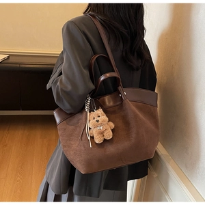 Large brown tote bag with suede paneling and bear charm shown from a side perspective