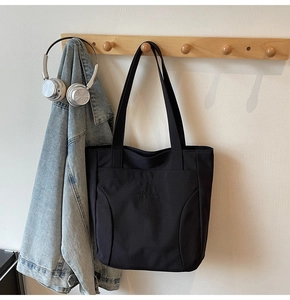 Close-up of a minimalist black tote bag featuring a practical front pocket and durable straps