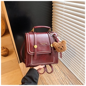 Detail of burgundy PU leather backpack with vintage metal buckle and plush bear charm