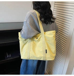 Rear view of a model wearing a light yellow large capacity nylon tote bag with outer pockets