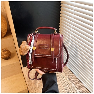 Detail view of burgundy leather backpack with white stitching and bear charm accessory