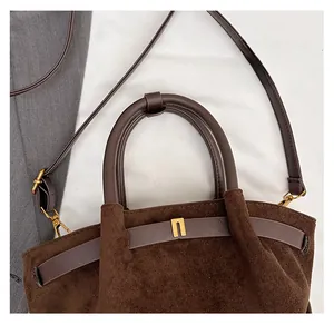 Close-up of brown matte suede handbag featuring golden bridge-shaped hardware and handles