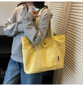 Detail view of the yellow nylon tote bag featuring front pocket and woven logo label
