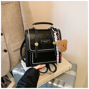 Close-up of black retro PU leather backpack with contrast stitching and bear charm