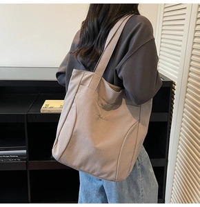 Detail of beige canvas tote bag with embroidered logo and dual shoulder straps
