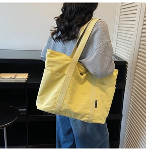 Side view of large yellow nylon tote bag with wide canvas shoulder straps on a model