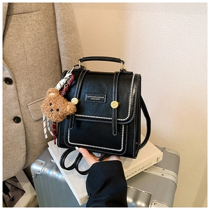 Detail of black leather backpack with white stitching and bear charm on white book
