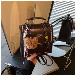 Detail of vintage dark brown PU leather bag with white stitching and bear charm