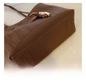 Detail view of woven brown tote bag featuring a reinforced bottom and stylish bead charm