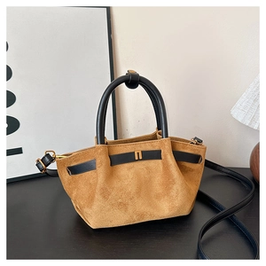 Detailed macro view of brown suede handbag featuring brass hardware and black leather handles