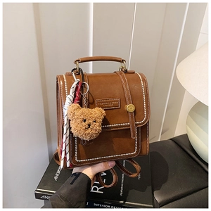 Close-up of a brown leather backpack with white stitching and a plush bear charm