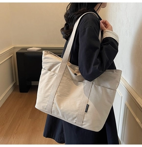 Detail of a large beige tote bag featuring a brand woven label and wide shoulder strap