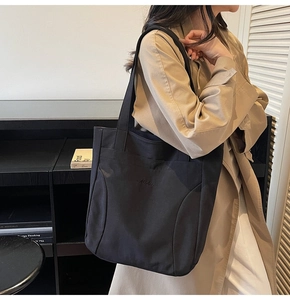 Detail of black nylon tote bag with embroidered logo on woman in beige trench coat
