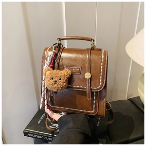 Close-up of vintage brown leather backpack with teddy bear charm and metal buckle