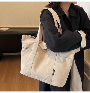 Close-up of beige canvas tote bag showing the side logo tag and front pocket detail