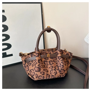 Close-up of leopard print fabric bag with brown leather straps and gold metal hardware