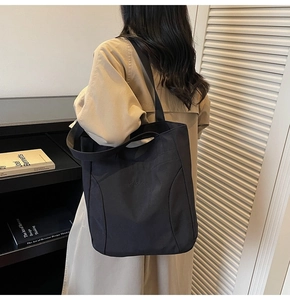 Detail of black canvas tote bag with shoulder straps worn by model in a modern room