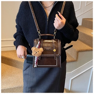 Detail of vintage brown leather handbag with contrast stitching and teddy bear charm