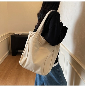 Detailed side view of cream canvas tote bag showing stitching and large front pocket