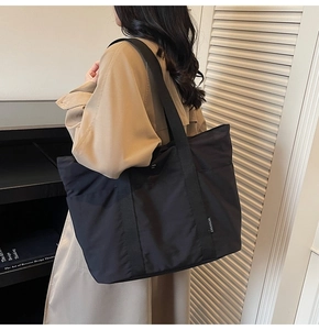 Close-up of black nylon tote bag featuring wide shoulder strap and side brand label