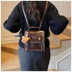 Detail of dark brown vintage backpack with contrast stitching and teddy bear charm