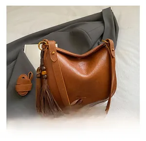 Detail of brown leather moon bag with tassel accent and adjustable gold hardware