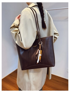 Detail of dark brown woven tote bag featuring a decorative beaded tassel and gold lettering