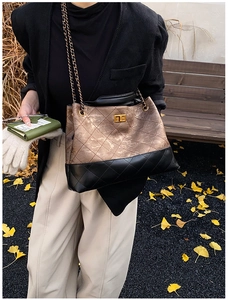 Detail of vintage quilted chain tote bag with golden lock on a wooden bench with autumn leaves