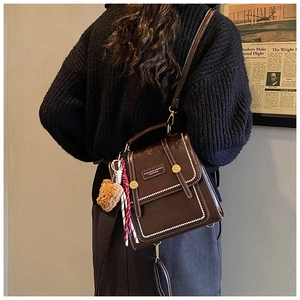Detail of a dark brown vintage backpack with white contrast stitching and bear charm
