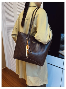 Detail of dark coffee tote bag with woven texture and ethnic beaded tassel charm