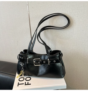 Detail of black glossy PU leather shoulder bag with buckle strap and key pendant decoration