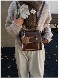 Detail of vintage brown leather crossbody bag with white stitching and cute bear charm