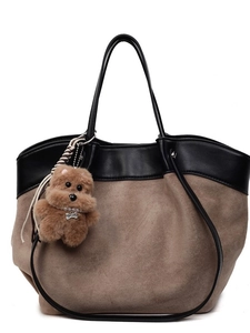 Brown suede tote bag with black leather handles and plush dog charm on white background