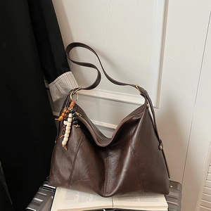Detail of dark brown leather tote bag with wooden bead tassel on travel suitcase