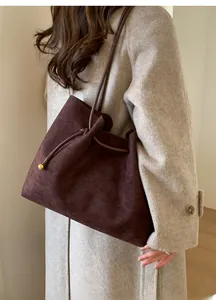 Detail of dark brown suede tote bag with drawstring closure and golden metal ball ornament