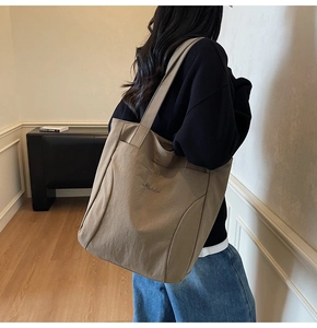 Detailed view of khaki canvas tote bag with elegant cursive embroidery and wide shoulder straps