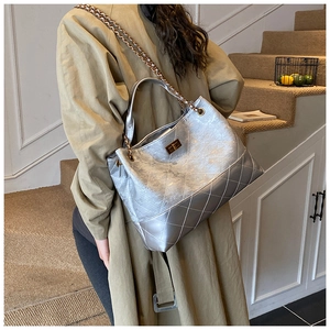 Detail of silver quilted chain bag with gold rotary lock worn by a model on stairs